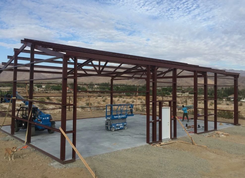 Red iron frames going up on a slab, with a scissor lift and boom lift on site.
