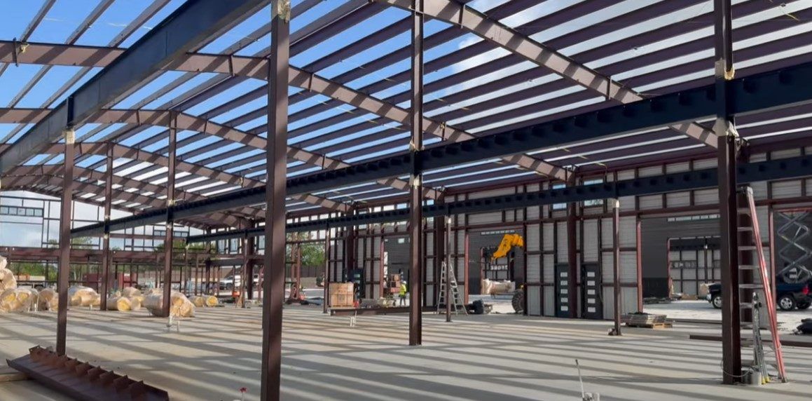 Rows of red iron frames and purlins standing over a large commercial slab.