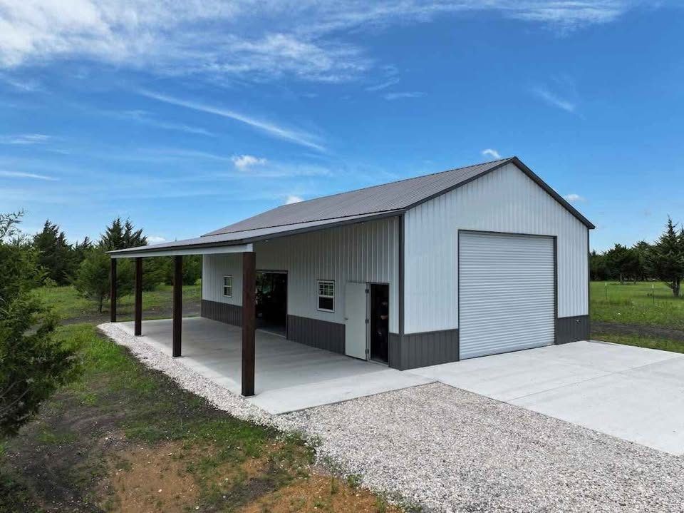 A white steel building with a tall roll-up door and an open lean-to for equipment along the side.
