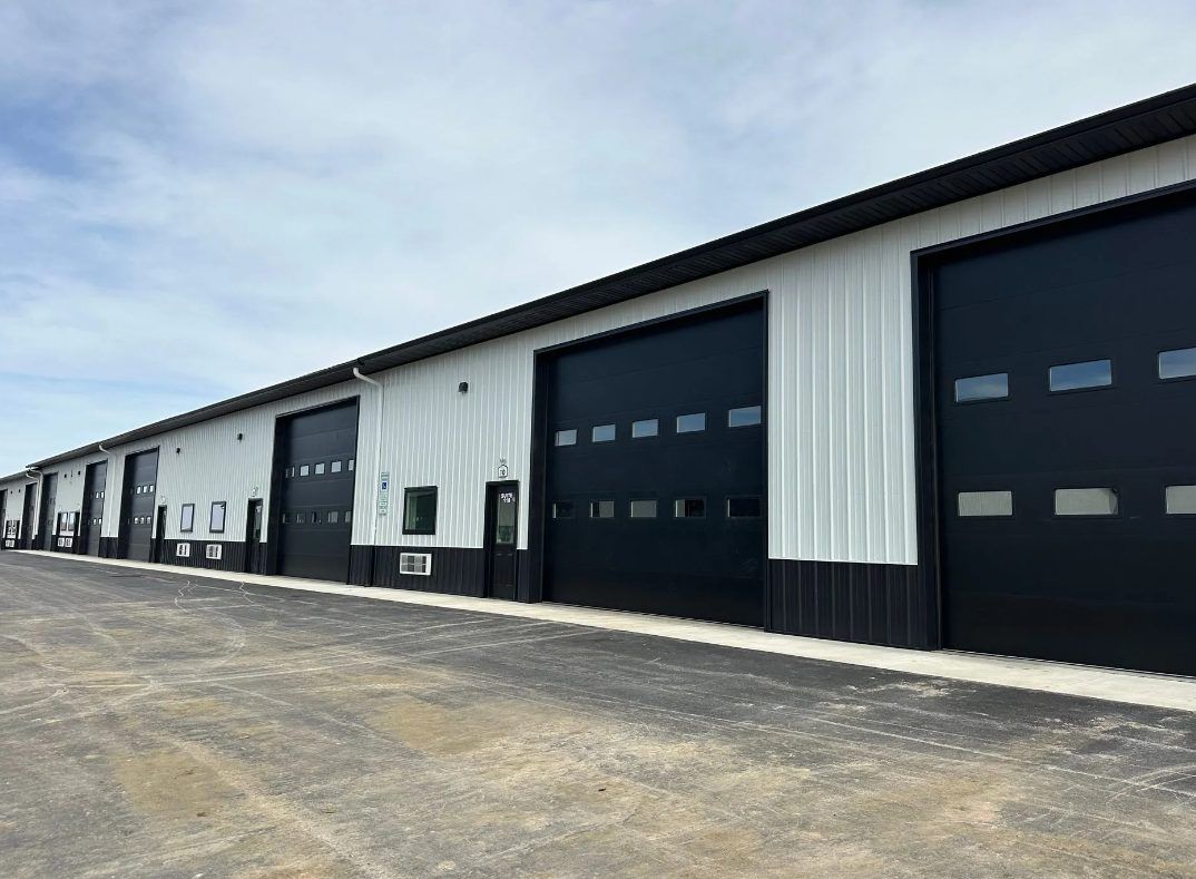 A long white and black steel building with a row of large overhead doors.